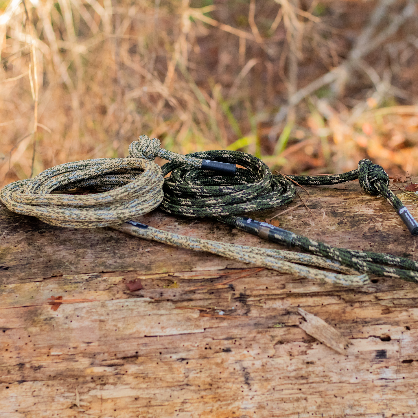 Preator Tether and Lineman's in both predator and Desert Camo sitting on a log